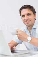 Smiling man with teacup using laptop at home