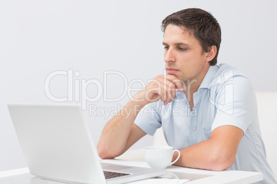 Serious young man using laptop at home