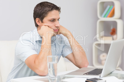 Serious young man using laptop in living room