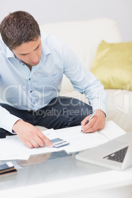 Young man with bills, calculator and laptop at home