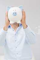 Casual man holding piggy bank in front of his face