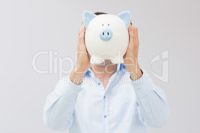 Casual man holding piggy bank in front of his face