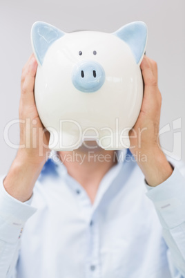 Casual man holding piggy bank in front of his face