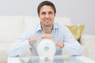 Handsome casual man with piggy bank in living room