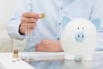 Mid section of a man putting some coins into a piggy bank