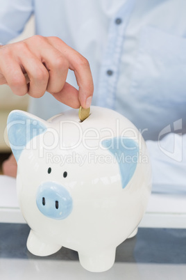 Close-up mid section of a man putting coin into piggy bank