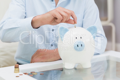 Mid section of a man putting some coins into a piggy bank