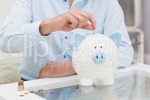 Mid section of a man putting some coins into a piggy bank