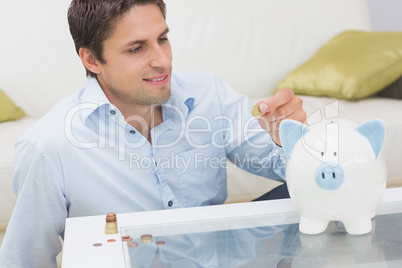 Casual man putting some coins into a piggy bank in living room