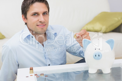 Casual man putting some coins into a piggy bank in living room