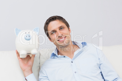 Handsome casual man with piggy bank in living room