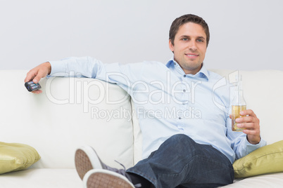 Relaxed man with a drink and remote control sitting on sofa at h