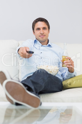 Man with a drink and remote control sitting on sofa