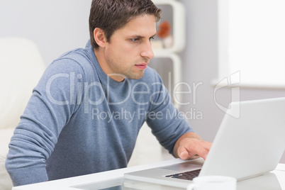 Serious young man using laptop in living room