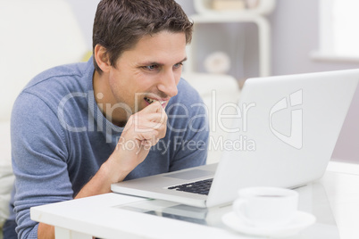 Thoughtful young man using laptop in living room