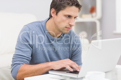 Serious young man using laptop in living room