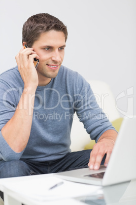 Man using cellphone and laptop in living room