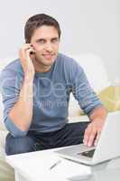 Smiling man using cellphone and laptop in living room