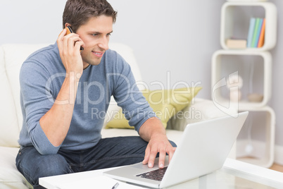 Smiling man using cellphone and laptop in living room