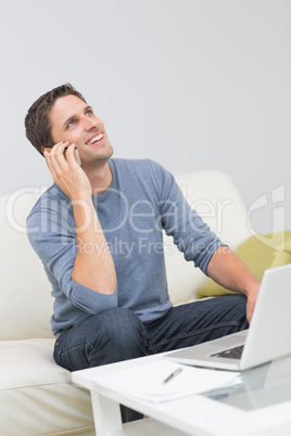 Cheerful man using cellphone and laptop in living room