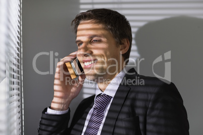 Businessman peeking through blinds while on call in office