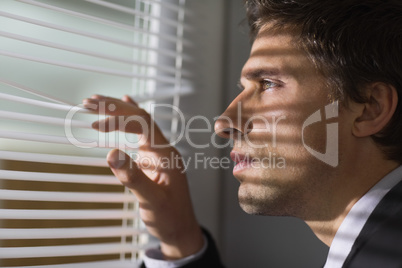 Serious businessman peeking through blinds in office