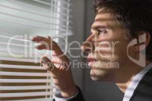 Serious businessman peeking through blinds in office