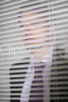 Businessman peeking through blinds in office