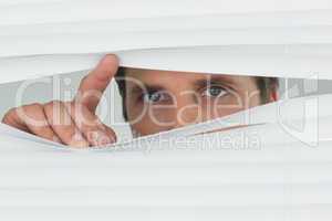 Close-up of green eyed businessman peeking through blinds