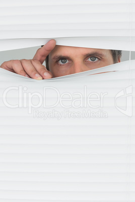 Green eyed businessman peeking through blinds