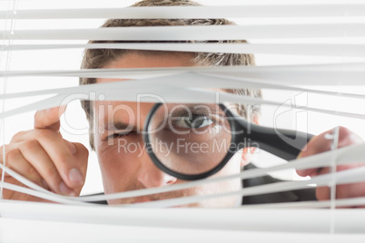 Businessman peeking through blinds with magnifying glass