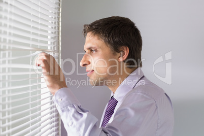 Businessman peeking through blinds in office