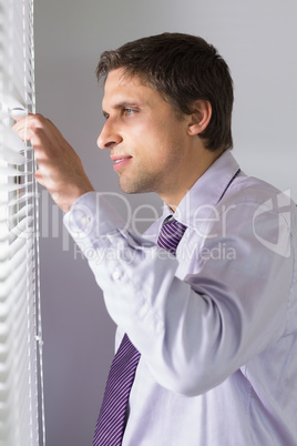 Businessman peeking through blinds in office