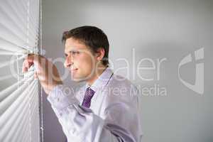 Businessman peeking through blinds in office