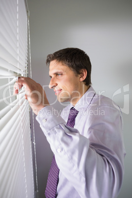 Young businessman peeking through blinds in office