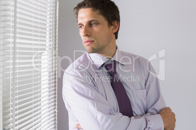 Serious businessman peeking through blinds in office