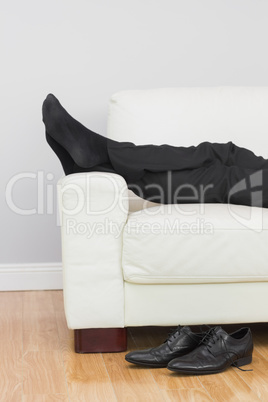 Low section of businessman resting on sofa in living room