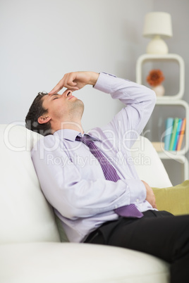 Tired businessman sitting on sofa in living room