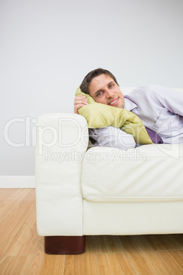 Smiling young businessman lying on sofa in living room