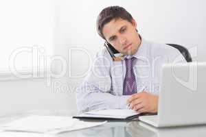 Businessman on call while writing in diary at office