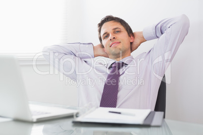 Relaxed businessman with hands behind head in office