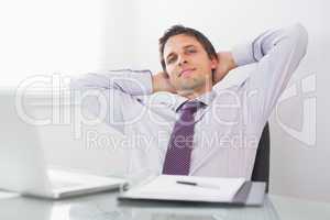 Relaxed businessman with hands behind head in office