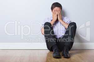 Businessman sitting on floor with hands covering face in empty r