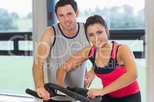 Trainer helping young woman work out at spinning class