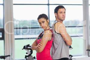 Serious young woman and man standing back to back in gym