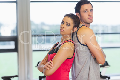 Serious woman and man standing back to back in gym