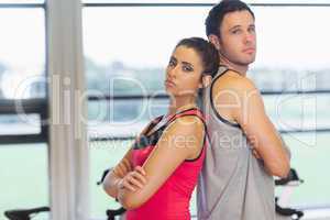 Serious woman and man standing back to back in gym