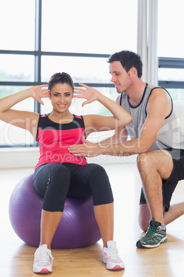 Trainer helping woman do abdominal crunches  on fitness ball