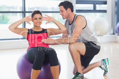 Trainer helping woman do abdominal crunches  on fitness ball