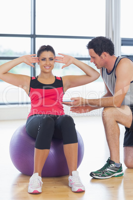 Trainer helping woman do abdominal crunches  on fitness ball